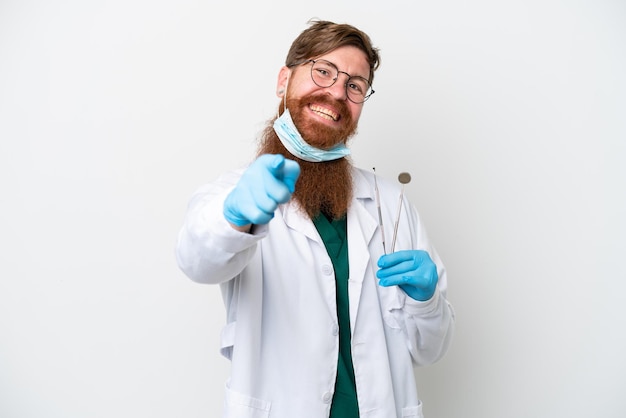 Dentiste homme rougeâtre tenant des outils isolés sur fond blanc pointant vers l'avant avec une expression heureuse