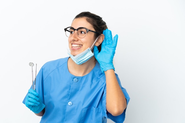 Dentiste de jeune femme tenant des outils isolés écoutant quelque chose en mettant la main sur l'oreille