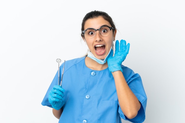 Dentiste de jeune femme tenant des outils isolés sur fond blanc avec une expression faciale surprise et choquée