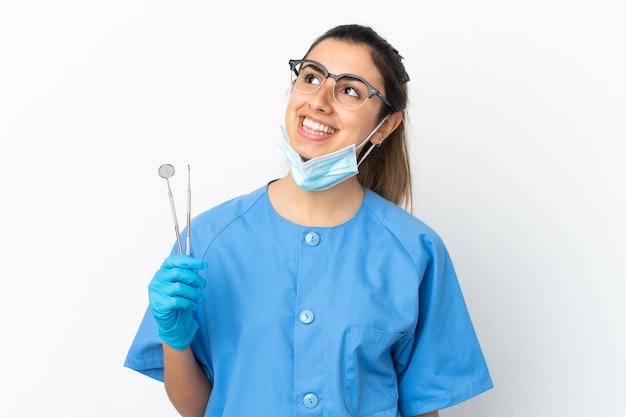 Dentiste de jeune femme tenant des outils isolés sur fond blanc pensant une idée tout en levant les yeux