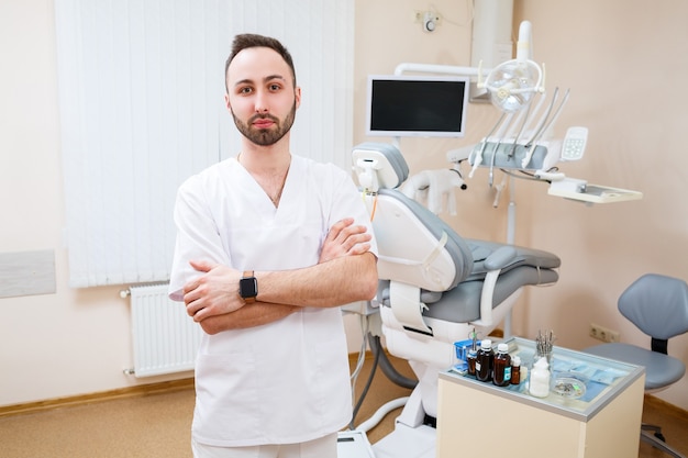 Dentiste sur le lieu de travail. Docteur barbu gai dans un bureau moderne spacieux et regardant la caméra avec un sourire aimable