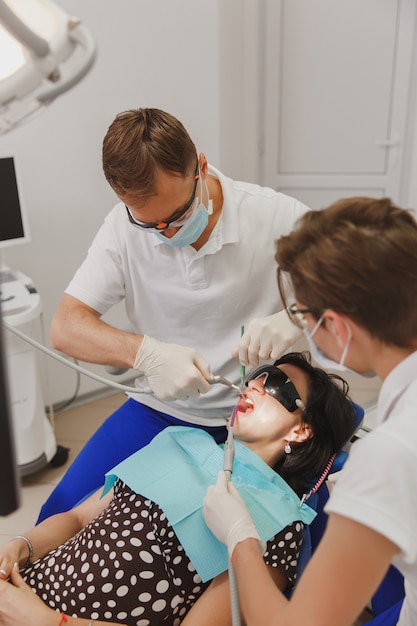 Le dentiste masculin avec une assistante aide à traiter les dents d'une patiente dans une clinique au bureau