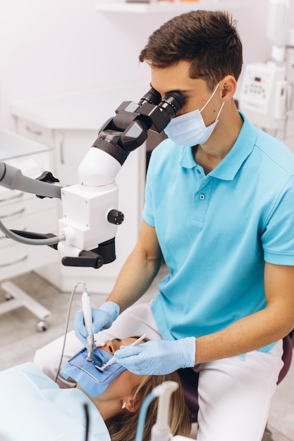 Dentiste masculin examinant une femme regardant sur les dents avec un microscope professionnel dans le cabinet dentaire de chirurgie