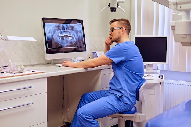 Dentiste masculin regardant la radiographie des dents sur l'ordinateur dans un cabinet de dentiste.