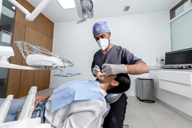 Dentiste masculin avec un uniforme debout tout en examinant la bouche d'une patiente dans une clinique dentaire