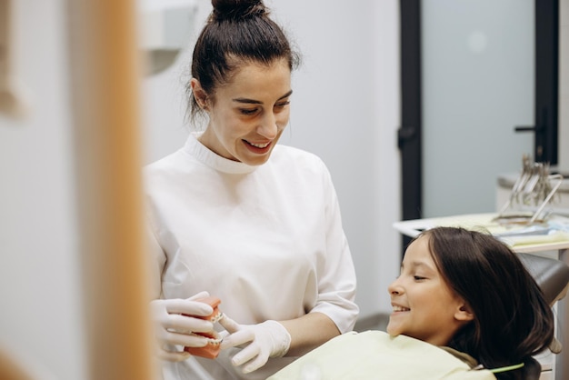 Dentiste montrant des accolades sur une fausse mâchoire à un enfant patient