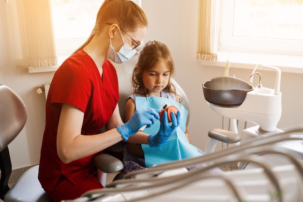Le dentiste montre à l'enfant comment utiliser correctement la brosse à dents pour se brosser les dents Modèle anatomique de la mâchoire brossage des dents Dentiste pédiatrique enseignant une leçon d'hygiène buccale pour les enfants en dentisterie