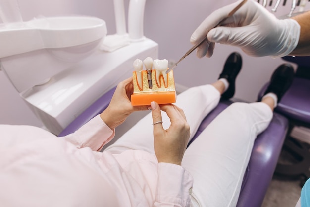 Le dentiste montre à la fille un modèle avec des dents parle d'implantation et de carie