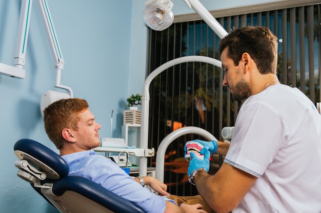 Le dentiste montre à son jeune patient une prothèse dentaire.