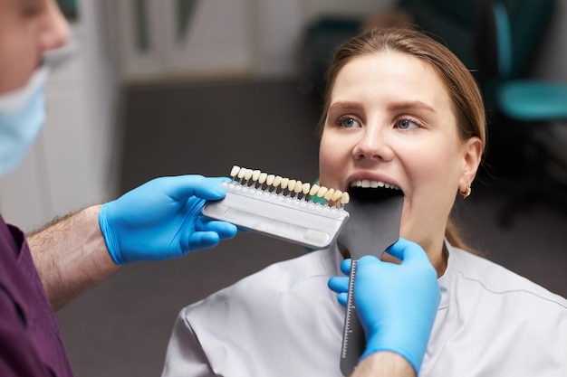 Dentiste orthodontiste utilisant un nuancier de dents choisissant la teinte des dents selon l'échelle Vita