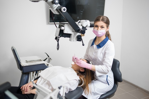 Dentiste avec outils dentaires - microscope, miroir et sonde traitant les dents d'un patient au bureau de la clinique dentaire