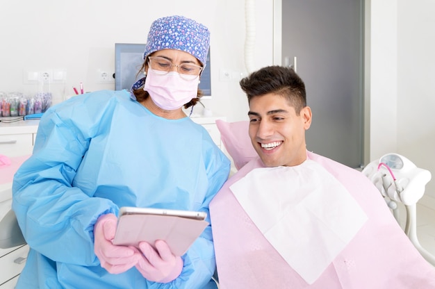 Dentiste et patient commentant des traitements dans une application de tablette dans une consultation avec un équip...