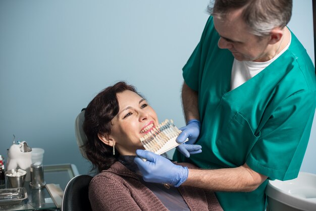 Un dentiste et une patiente vérifiant et sélectionnant la couleur des dents dans un cabinet de dentiste