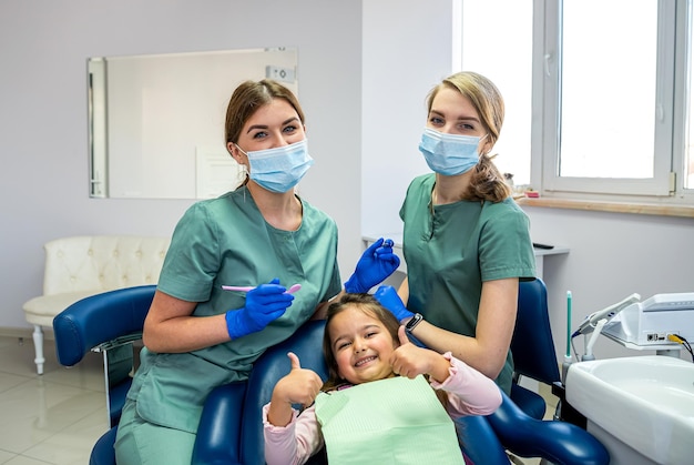 Dentiste pédiatrique avec assistant avec une patiente enfant montrant les pouces vers le haut