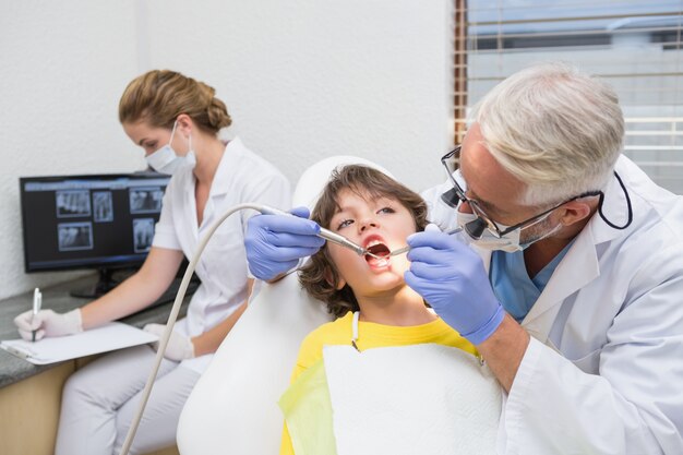 Dentiste pédiatrique examinant les dents d&#39;un petit garçon avec un assistant derrière