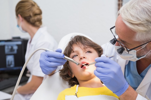 Dentiste pédiatrique examinant les dents d&#39;un petit garçon avec un assistant derrière