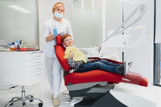 Dentiste pédiatrique examinant les dents d'un petit garçon dans le fauteuil des dentistes à la clinique dentaire