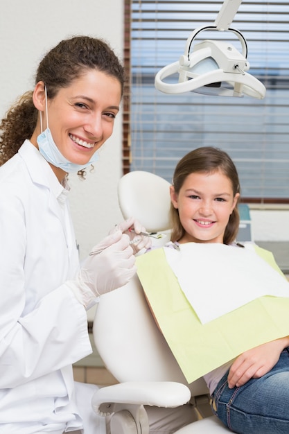 Dentiste pédiatrique et petite fille dans la chaise des dentistes, souriant à la caméra