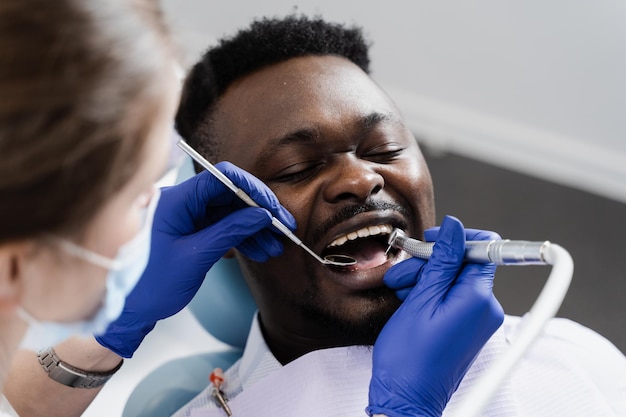 Photo le dentiste perce les dents et enlève les caries d'un homme africain dans une clinique dentaire traitement des dents remplissage dentaire pour un patient afro-américain