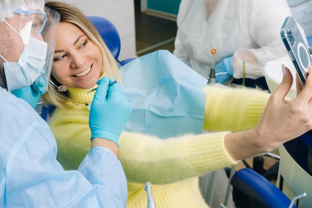 Un dentiste portant un masque de protection est assis à côté d'un patient et prend une photo de selfie tout en travaillant