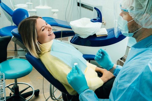 Un dentiste portant un masque de protection est assis à proximité et tient des instruments dans ses mains avant de traiter un patient au cabinet dentaire.