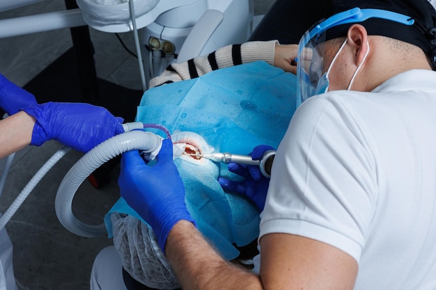 Un dentiste professionnel examine les dents d'un patient avec un équipement dentaire et tient des instruments dentaires près de sa bouche Dentiste Cabine dentaire