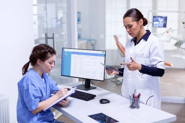 Dentiste racontant le diagnostic des dents d'un patient infirmier tenant une radiographie dans une clinique dentaire. Assistant de stomatologie et docteur en dents discutant à la réception du cabinet dentaire