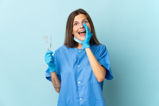 Dentiste slovaque tenant des outils isolés sur fond bleu en criant avec la bouche grande ouverte