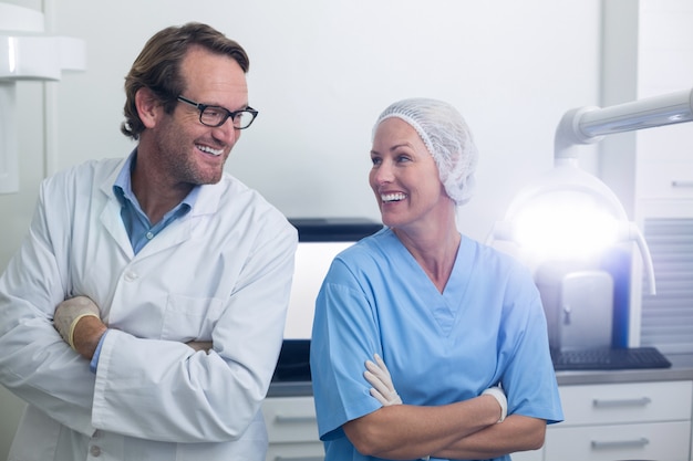 Dentiste souriant et assistant dentaire debout avec les bras croisés