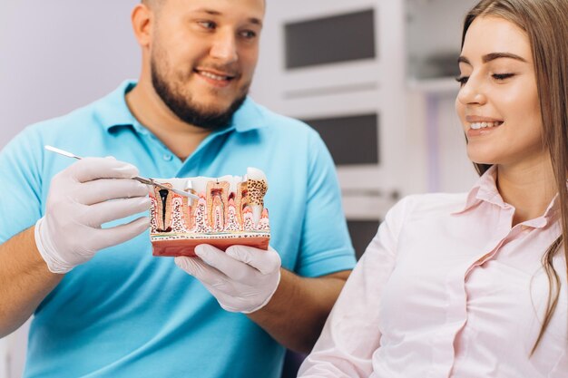 Le dentiste sourit et montre à la fille un modèle avec des dents parle d'implantation et de carie