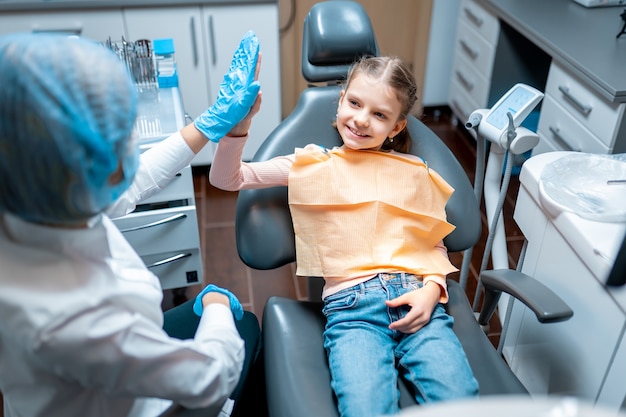Dentiste sympathique donnant cinq petits patients assis sur un fauteuil dentaire après examen