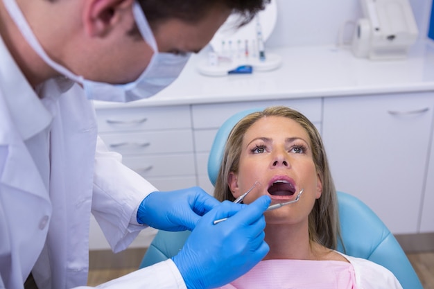 Dentiste tenant des outils lors de l'examen de la femme à la clinique médicale