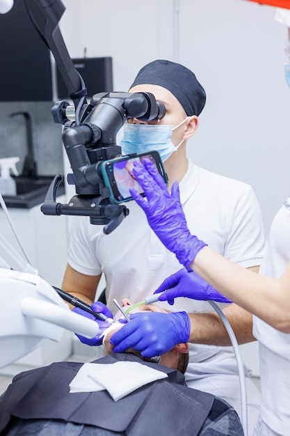 Un dentiste traite les dents à l'aide d'un microscope dentaire et d'outils L'assistant tient une seringue avec de l'air et de l'eau Cabinet dentaire