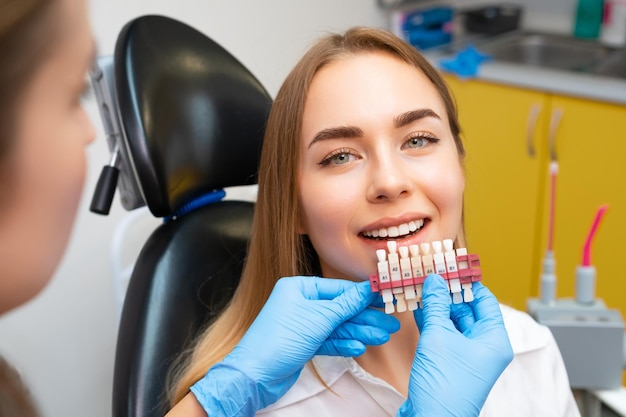 Photo le dentiste utilise un ensemble d'implants avec diverses nuances de tonalité pour le blanchiment des dents d'une jeune femme