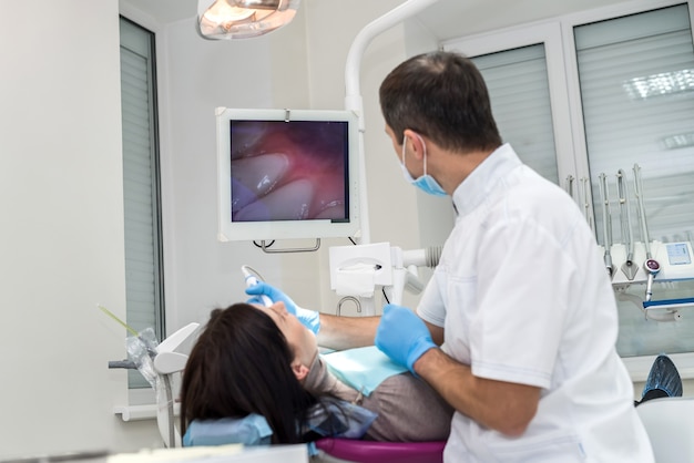 Dentiste vérifiant les dents du patient avec caméra, à la recherche sur l'écran