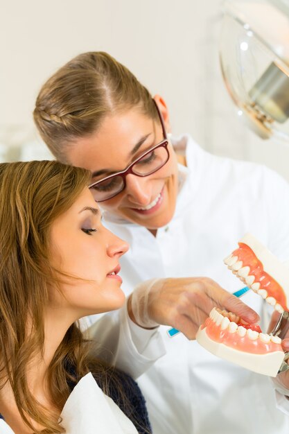 Dentisthis la chirurgie tient une prothèse et explique une patiente avec une brosse à dents