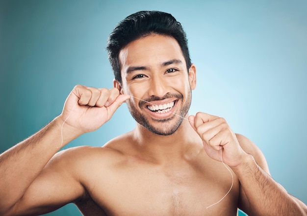 Dents de bien-être et soie dentaire portrait d'un homme avec nettoyage et santé dentaire dans un studio Face fond bleu et personne masculine en bonne santé avec soie pour l'hygiène buccale et les soins de santé avec un sourire