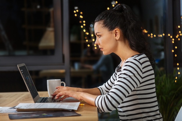 Dépendance au travail. Femme sérieuse intelligente travaillant dur assis à l'ordinateur portable et en tapant tout en étant concentrée sur son travail