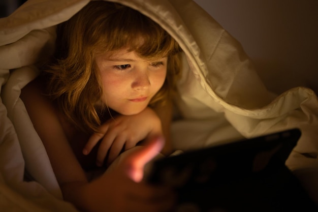 Dépendance aux gadgets pour enfants et insomnie enfant lit l'ebook petit garçon regarde l'écran du tabl