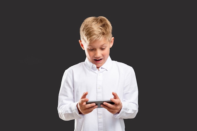 Dépendance aux jeux mobiles. Stress anxiété. Garçon choqué perdant en jouant au téléphone isolé sur un mur gris.