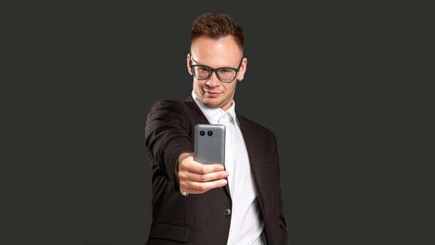 Dépendance aux médias sociaux Technologie moderne Homme d'affaires confiant prenant selfie sur téléphone isolé sur fond noir espace copie flou Communication en ligne Application mobile