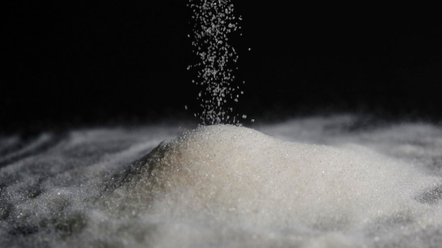 Déplacer des grains de sucre tombant dans une montagne de sucre. Beaucoup de sucre sur fond noir