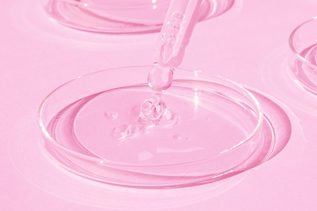 Déposer du gel d'une pipette dans une boîte de Pétri sur fond rose Huile de rétinol de gel de sérum de laboratoire cosmétique