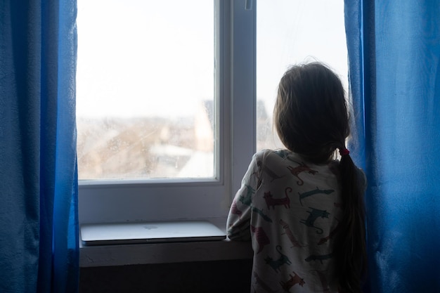 La dépression des enfants. Malheureuse petite fille assise se sentant seule près de la fenêtre se serrant dans ses bras à la maison. Copiez l'espace.