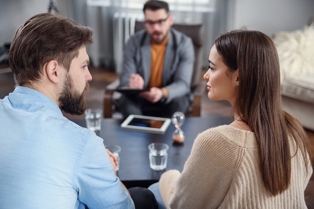 Déprimé Jeune Couple D'homme Et Femme Parlant Avec Un Psychologue En Séance De Thérapie Dans Un Bureau Moderne. Mauvaises Relations Sans Avenir.