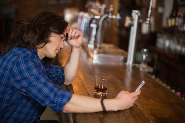 Déprimé jeune homme à l'aide de mobile au pub