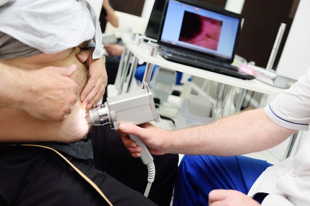 Le dermatologue examine les grains de beauté ou l'acné du patient avec un dermatoscope. Prévention du mélanome