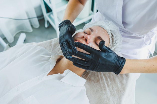 Un dermatologue traite le visage d'une femme allongée sur une table de massage Soin de la peau du visage Une esthéticienne applique un masque au visage de la femme