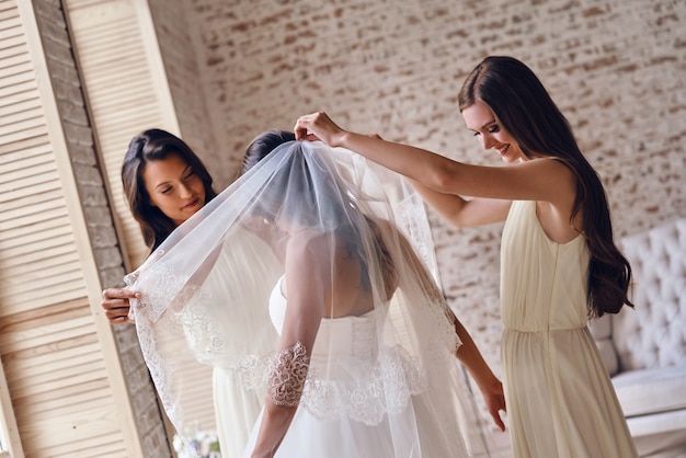 Derniers préparatifs. Demoiselles d'honneur aidant la mariée à mettre un voile en se tenant debout dans la cabine d'essayage