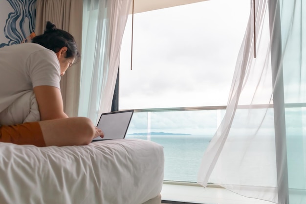 Derrière l'angle de l'homme travaille sur le lit avec vue sur la mer concept de workation